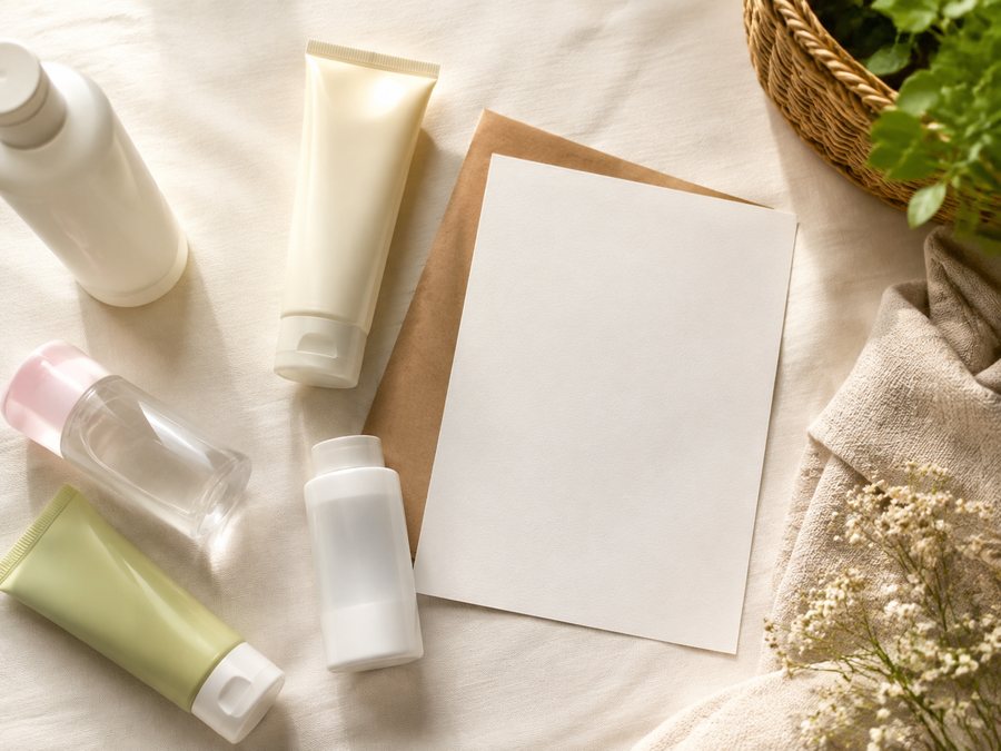 a flat lay of ordinary drugstore beauty bottles and tubes next to a blank price-list card, soft top light